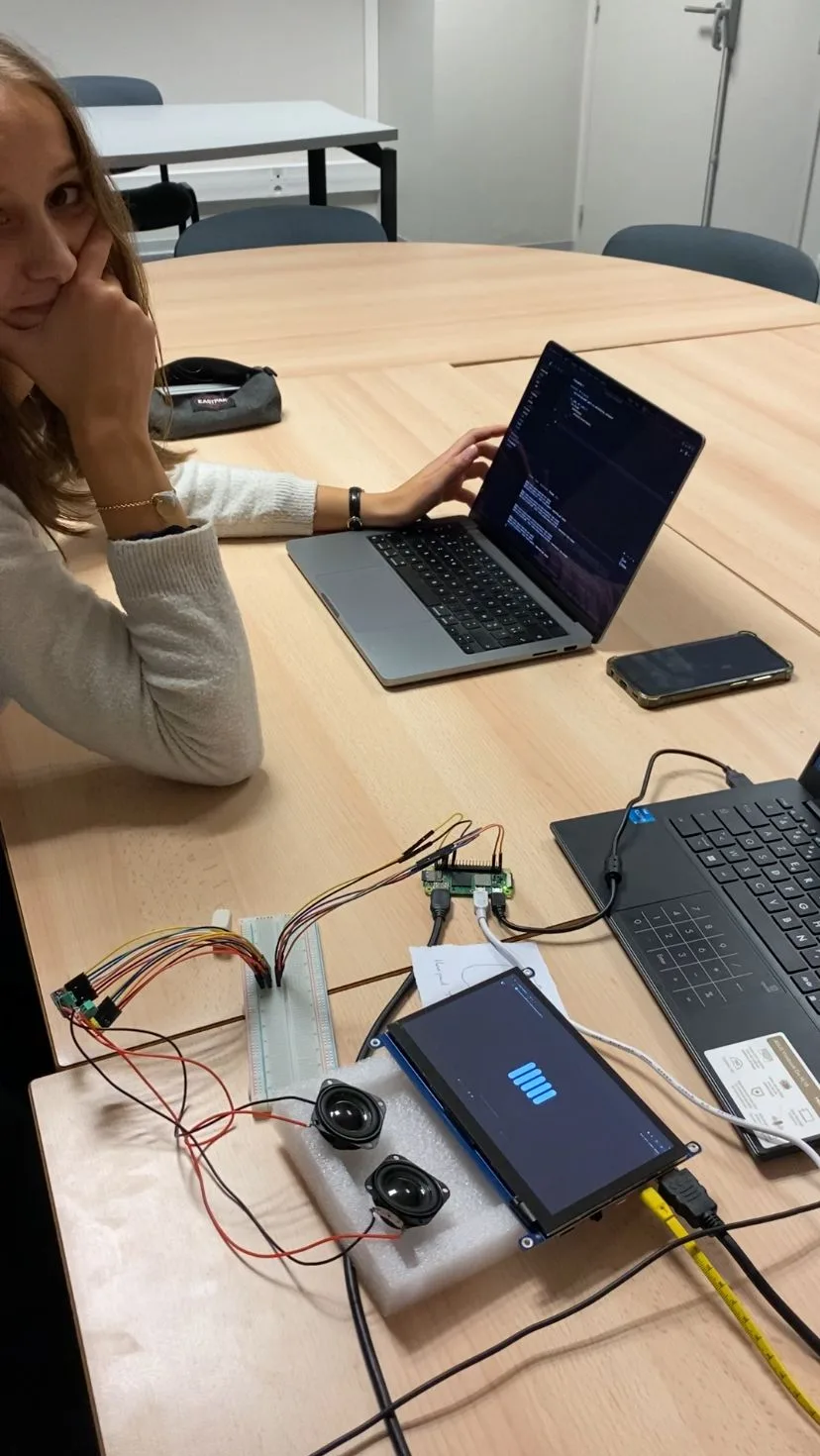 Accoudée à la table, l’air très satisfaite, à côté du premier montage d’Orion qui fonctionne : Raspberry Pi, haut-parleurs et écran allumé